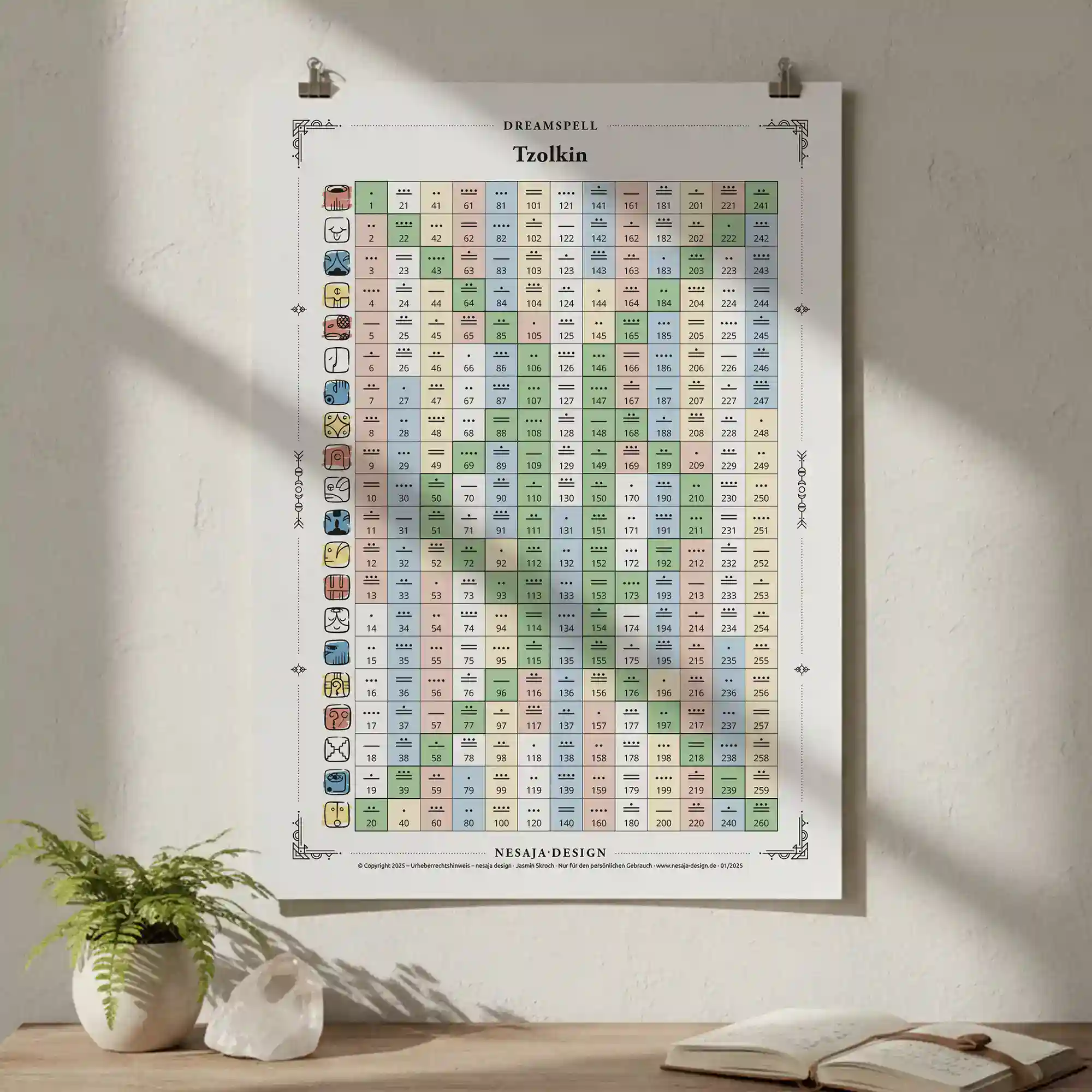 Tzolkin-Kalenderposter im weißen Rahmen, aufgehängt an einer hellen Wand. Davor stehen eine Vase mit zarten Trockenblumen und ein geöffnetes Buch auf einem schmalen Holzbrett. Sonnenlicht wirft sanfte Schatten auf die Szene