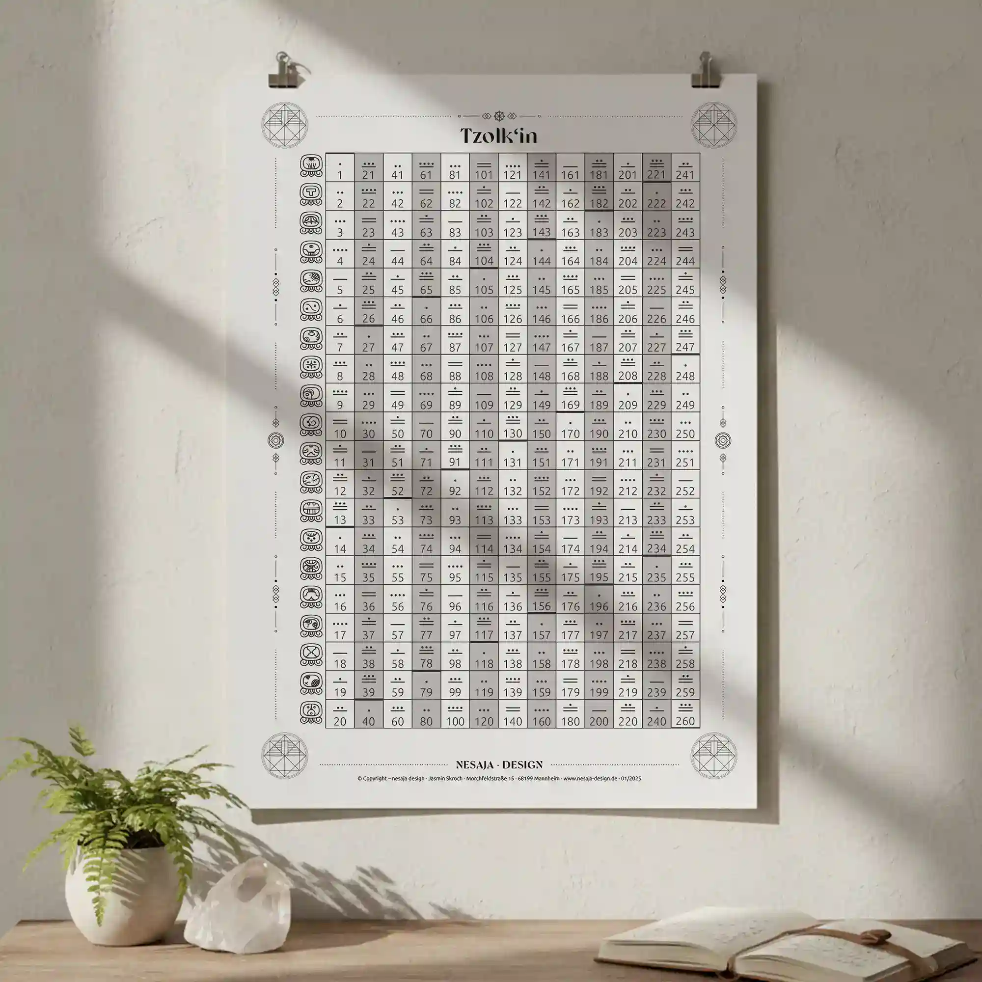Schwarz-weißes Tzolkin-Poster im weißen Rahmen, aufgehängt an einer hellen Wand. Sonnenlicht fällt seitlich hinein und wirft sanfte Schatten; darunter stehen ein paar Bücher und eine dekorative Vase.